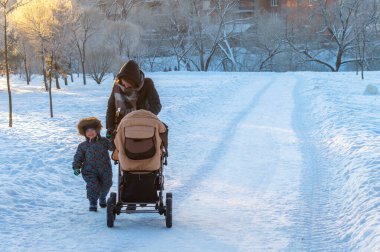 Kış akşamı parkında çocuklu bir kadın ve bebek arabası.