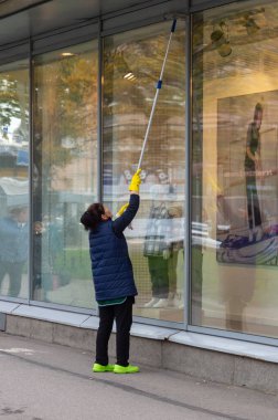 Kadın dükkanın camını temizliyor.