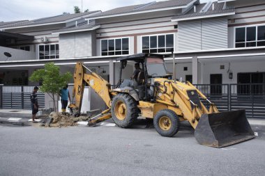 Perak, Malezya. 1 Aralık 2021: Su işçisi ve traktörü, Taman Mas 1 Kampong Koh 'taki boru tamiri için asfalt caddesinden toprak çıkardı.