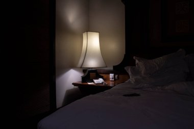 Odada parlayan karanlık başucu lambası.