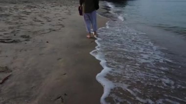 unrecognizable lady barefooted strolling along the beach.