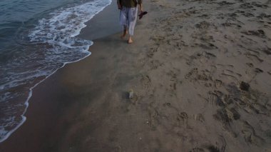 unrecognizable lady barefooted strolling along the beach.