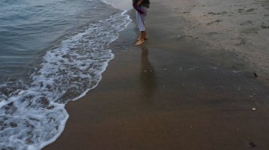 Tanımlanamayan bir kadın plajda yalınayak geziniyor..