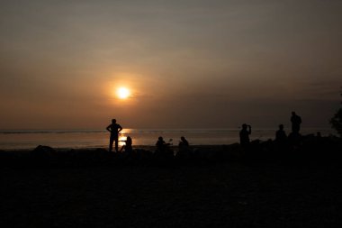 unrecognizable people standing in the dark viewing the evening setting sun.