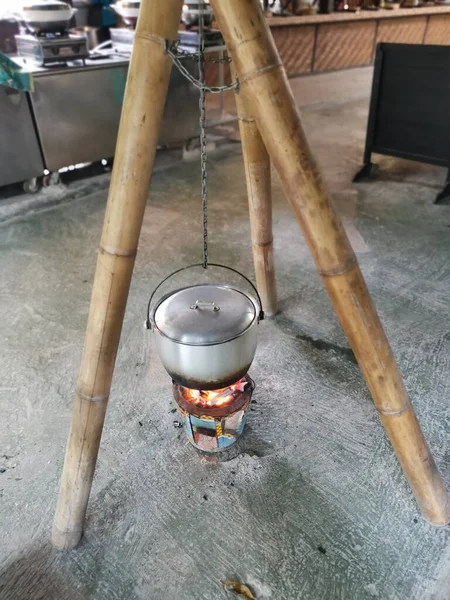 鍋ストーブの上で竹の棒の料理に掛かるハンドル付きアルミ調理鍋 — ストック写真
