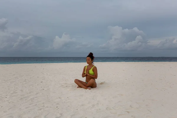 Ein junges attraktives Mädchen in Sportuniform, im Bikini macht Yoga am Strand am Meer, bei Sonnenuntergang. Hintergrund blaues Meer und Himmel — Stockfoto