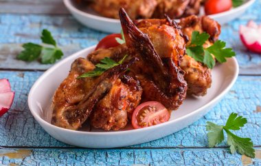 Mavi arka planda beyaz bir tabakta kızarmış tavuk kanadı.