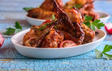 Mavi arka planda beyaz bir tabakta kızarmış tavuk kanadı.