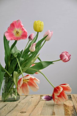 Bir demet parlak renkli lale. Tahta bir masadaki cam vazoda duran güzel bahar çiçekleri. Kadınlar günü için yumuşak bir buket.