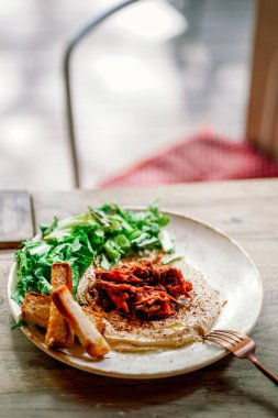 Sebzeli lezzetli humus ve açık hava restoranındaki ahşap bir masada ekmek. Akdeniz atıştırması, vejetaryen sağlıklı gıda konsepti. Avrupa vejetaryen yemeği. Evcil