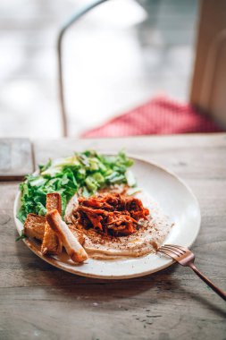 Sebzeli lezzetli humus ve açık hava restoranındaki ahşap bir masada ekmek. Akdeniz atıştırması, vejetaryen sağlıklı gıda konsepti. Avrupa vejetaryen yemeği. Evcil