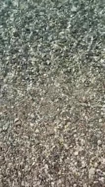 Crystal clean turquoise waves of Adriatic sea in sunny morning. Sunbeams on transparent  sea water and pebble. Calmness of seashore. Summer vibes on vacation. Natural meditation through the water