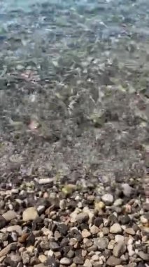 Crystal clean turquoise waves of Adriatic sea in sunny morning. Sunbeams on transparent  sea water and pebble. Calmness of seashore. Summer vibes on vacation. Natural meditation through the water