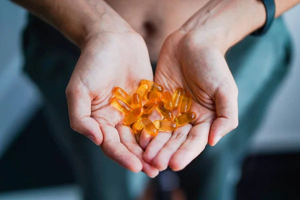 A handful of vitamins in the hands of a young man. Bright Omega-3 capsules. Medicinal product of animal origin. Fish fat source of vitamins A and D. Healthy lifestyle