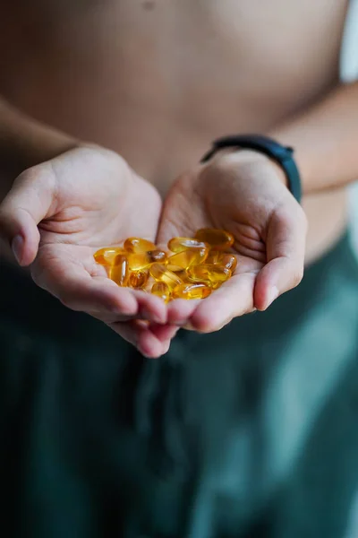 A handful of vitamins in the hands of a young guy in the form of heart. Bright Omega-3 capsules. Medicinal product of animal origin for healthy lifestyle. Fish fat source of vitamins A and D