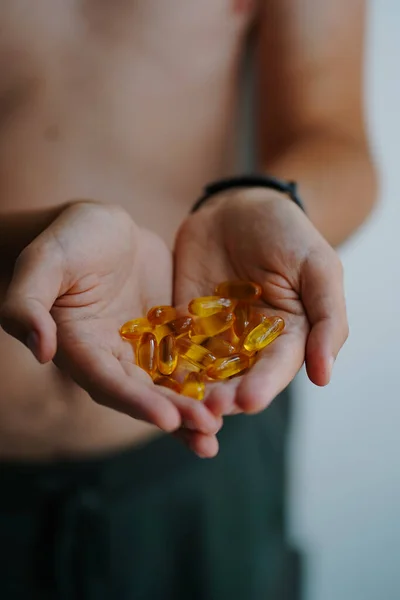 A handful of bright capsules of food supplemens in the hands of a young man in the morning. Omega-3 close up. Medicinal product of animal origin. Fish oil source of vitamins A and D. Healthy lifestyle