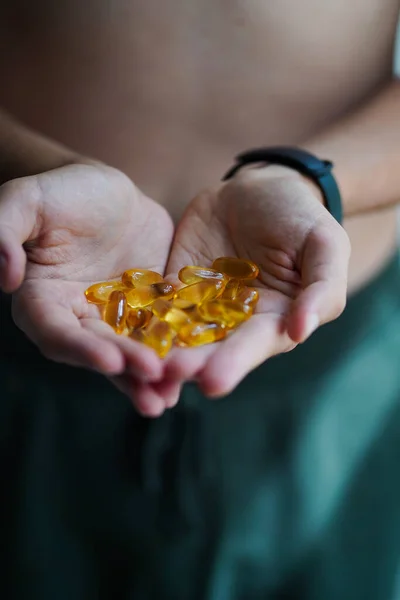 A handful of food suplements in the hands of a young guy in the form of heart. Bright Omega-3 capsules. Medicinal product of animal origin for healthy lifestyle. Fish fat source of vitamins A and D