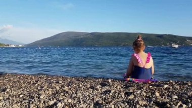 A little girl sits on shore of Adriatic Sea and looks into distance, Lazure Beach, Herceg Novi, Montenegro