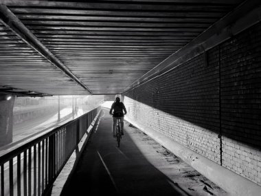 Işıklar ve gölgelerle dolu bir köprüde bisiklete binen bir adamın siyah beyaz fotoğrafı. 