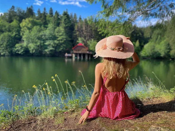 Woman Pink Dress Hat Sitting Lake Admiring View — Stockfoto