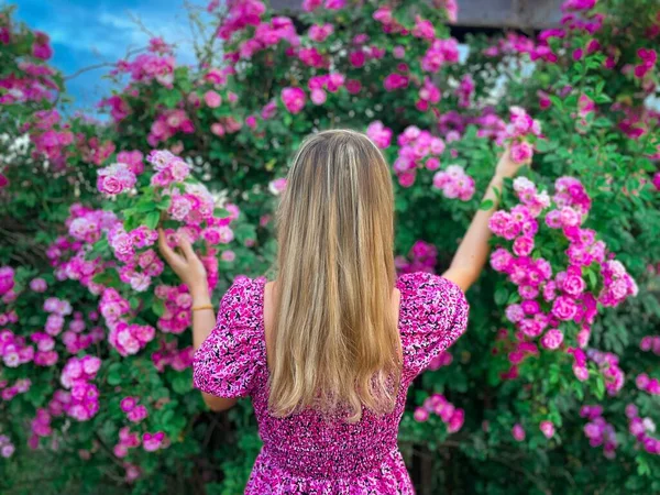 Arka tarafta uzun sarı saçlı genç bir kadın var. Bahçeden pembe güller alıyor.