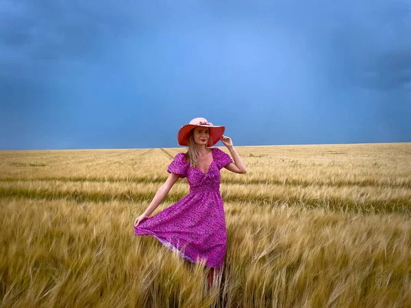 Woman in pink dress and hat in a field of wheat on a cloudy and stormy summer day