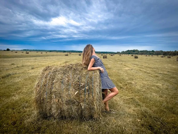 Woman standing near haystack on a field and dark storm clouds in the sky