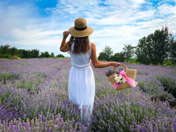 Rear view of woman in white dress wearing a straw hat standing in a field of lavender