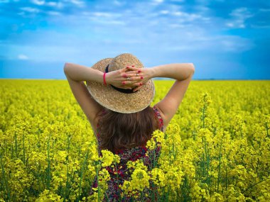Woman wearing straw hat in a field of canola flowers on a sunny day with blue sky