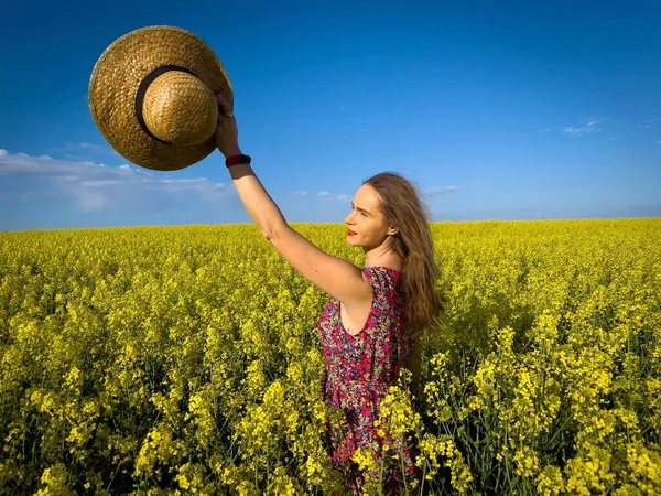 Yazlık elbiseli kadın kollarını kaldırıp kanola çiçeklerinden bir tarlada dikiliyor.