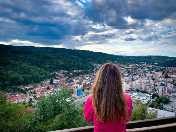 Rear view of woman standing near the railing and  looking down at the city on a cloudy day