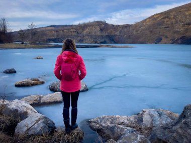 Rear view of woman with backpack standing near a frozen lake in the mountains