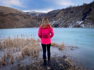 Rear view of woman with backpack standing near a frozen lake in the mountains