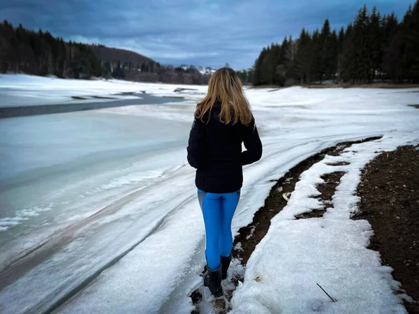 Rear View Woman Wearing Winter Clothes Standing Frozen Lake Surrounded 免版税图库图片