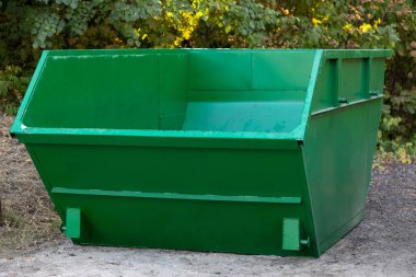 İnşaat için boş büyük yeşil metal konteynır ya da parktaki ağaçların arka planına karşı diğer büyük çaplı çöpler. Çevre koruma kavramı