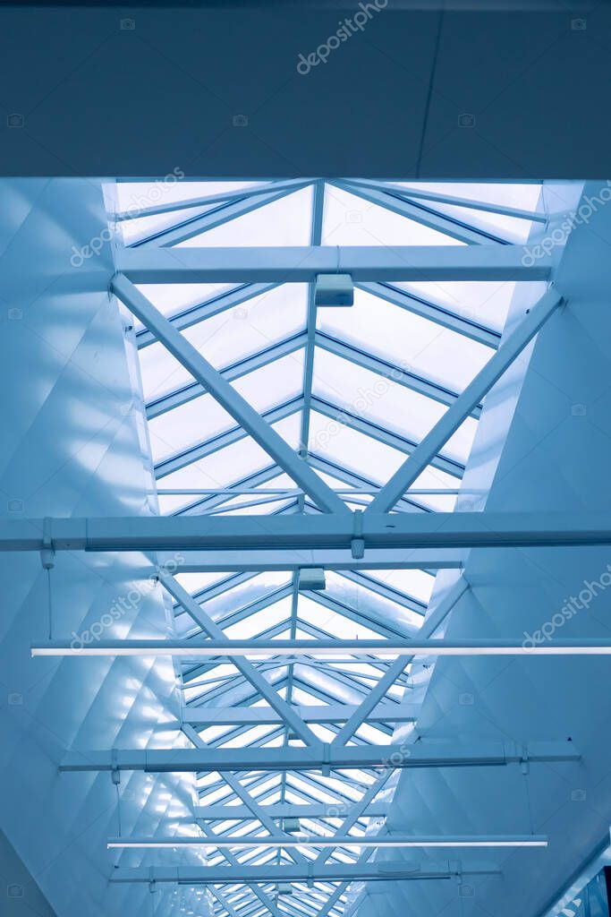 Steel frame of the glazed roof of a warehouse, shopping or office center against a blue sky. The ceilings are made of metal beams interconnected by welding to maintain rigidity.