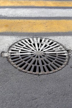Yaya geçidi işaretli asfalt yolda kanalizasyon kapağı. Dikey