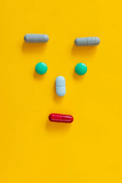 minimalistic image of a human face from pills and pills on yellow background. Vertical