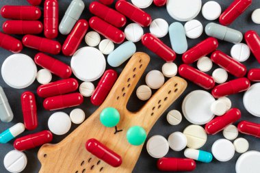 Bir sürü hapın, hapın ve vitaminin arka planında yeşil haptan gözleri olan tahta bir tavşan. Uyuşturucu veya ilaç bağımlılığı kavramı
