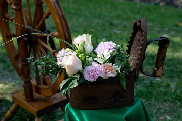 美丽的玫瑰花束和康乃馨在生锈的老式铁中 背景为木制纺车 商业或住宅空间的最新设计 旧物的第二人生 — 图库照片