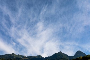 Gün doğumunda dağların üzerinde tüylü bulutlarla yüksek mavi gökyüzü