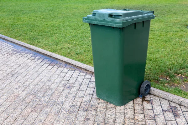 Plastic green garbage can for collecting garbage in the park. Mobile trash can with wheels. Close-up