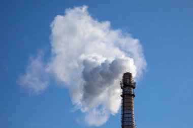 Fabrika bacası kış boyunca mavi gökyüzü arka planındaki borudan duman üflüyor. Hava kirliliği ve eski sanayi enerji santralinin yol açtığı küresel ısınma