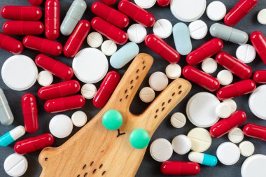 Bir sürü hapın, hapın ve vitaminin arka planında yeşil haptan gözleri olan tahta bir tavşan. Uyuşturucu veya ilaç bağımlılığı kavramı