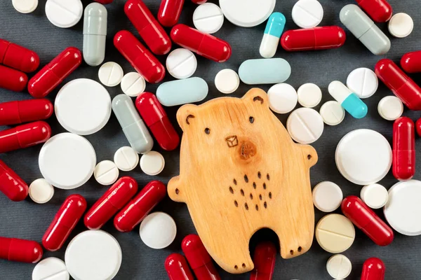Pek çok hapın, hapın ve vitaminin arka planında bulunan tahta bir ayı yavrusu. Çocuk ilaçları, çocuk tedavileri.