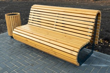 Yeni bir yerleşim bölgesinde, ahşap çıtalardan yapılmış, modern, rahat bir ahşap bank ve çöp tenekesi. Ev arazisinin peyzajı.