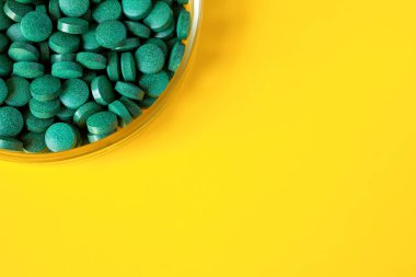 Parlak sarı arka planda, petri kabında bir sürü yeşil hap var. Boşluğu kopyala