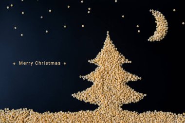 Çiğ yumurtalı makarnadan yapılmış mutlu noel tebrik kartı tasarımı: Noel ağacı, yıldızlı gökyüzü, ay ve siyah arka planda yazan Mutlu Noeller. Kış sanatı veya çocuk yaratıcılığı konsepti