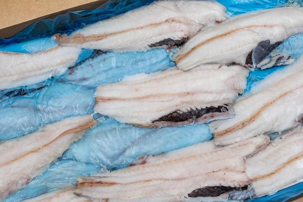 frozen fish Longtail hake in a box. Packaging with interleave plastic film and fish. Argentine tradel fish after primary processing is ready for sale. Close-up