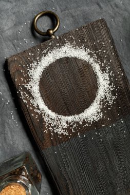 Eski ahşap bir tahtanın üzerinde yuvarlak tuz çerçevesi. Mutfak teması için metal dekoratif elementler var. Çapraz düzenleme. Dikey. Boşluğu kopyala